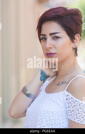 Belle jeune femme avec papillon tatouage au poignet cou toucher la main à l'extérieur Banque D'Images