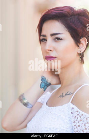 Belle jeune femme avec papillon tatouage au poignet cou toucher la main à l'extérieur Banque D'Images