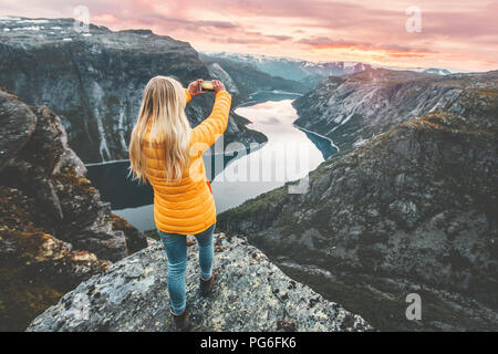 Woman taking photo par smartphone sur falaise de montagne sur le lac de voyager en Norvège vie aventure vacances actives La technologie moderne connection con Banque D'Images