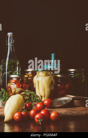 Les bocaux en verre avec des légumes en conserve et des légumes frais sur la table Banque D'Images