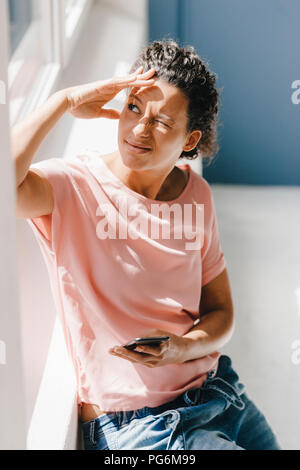 Woman holding smartphone, scintillent dans la lumière du soleil Banque D'Images