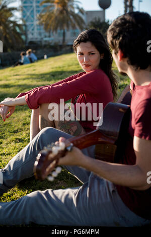 Espagne, Barcelone, jeune femme assise sur un pré à regarder petit ami jouer de la guitare Banque D'Images