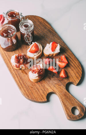 Vue de dessus de planche à découper, la confiture de fruits en pots et des sandwichs au fromage à la crème et confiture sur la table de marbre Banque D'Images