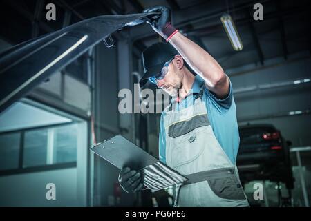 Problème de moteur du véhicule. Portrait d'un technicien dans son 30s à l'intérieur de la zone de service concessionnaire prendre inspection détaillée sous un capot de voiture. L'industrie automobile. Banque D'Images