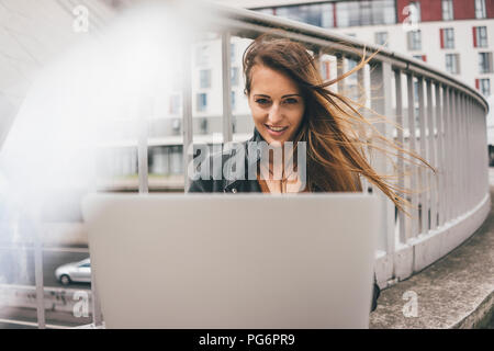 Portrait de jeune femme avec les cheveux balayés par l'utilisation de l'ordinateur portable sur pont de l'autoroute Banque D'Images