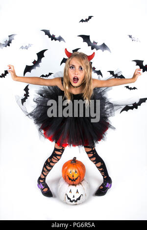 Petite fille avec un démon costume habillé en noir robe rouge et red devil horns pour citrouille et Halloween Party, qui posent avec plaisir smi Banque D'Images