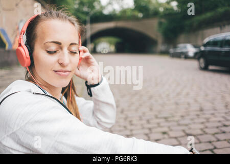 Sportive Smiling young woman with closed eyes portant des écouteurs à l'extérieur Banque D'Images