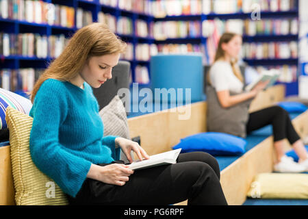 Teenage Girls sitting in a public library reading book Banque D'Images