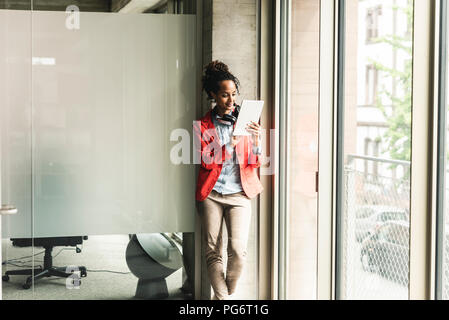 Jeune femme avec un casque debout dans couloir, using digital tablet Banque D'Images