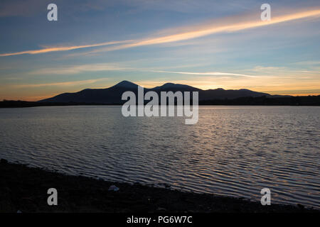 Silhouette de la Mourne Mountains au coucher du soleil avec des stries de couleur dans le ciel et mer à la baie de Dundrum en premier plan. Banque D'Images