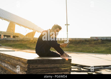 L'homme au casque assis sur la pile de bois, using smartphone Banque D'Images