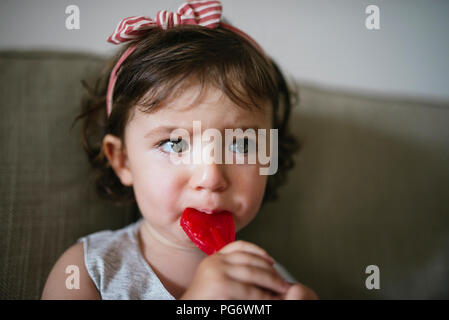 Cute baby girl eating une sucette en forme de coeur à la maison Banque D'Images