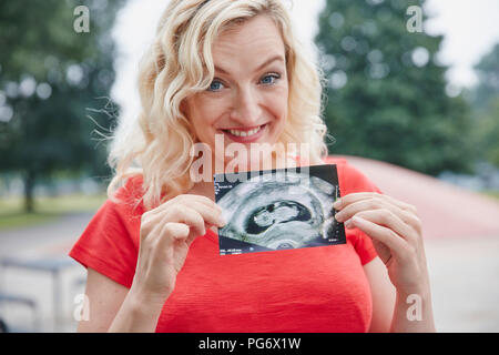 Portrait of happy pregnant woman holding ultrasound image extérieur Banque D'Images