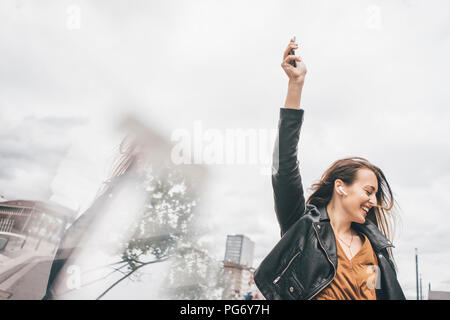 Happy young woman with in-ear téléphones cellulaires et Banque D'Images