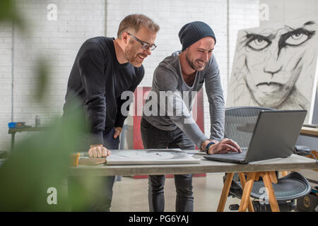 Ordinateur portable à l'aide de l'artiste souriant avec l'homme en studio Banque D'Images