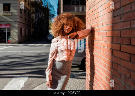 Portrait de la belle jeune femme à la coiffure afro appuyé contre un mur de briques dans la ville Banque D'Images