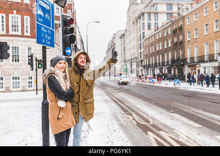 UK, Londres, jeune couple standing at roadside hailing taxi en hiver Banque D'Images