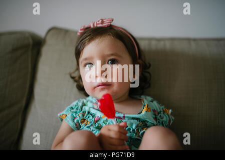 Cute baby girl eating une sucette en forme de coeur à la maison Banque D'Images