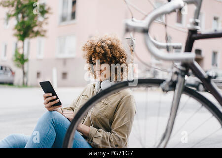 Femme dans la ville avec des écouteurs, using smartphone Banque D'Images