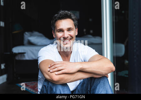 Portrait of smiling man en pyjama à la maison assis à la fenêtre Français Banque D'Images