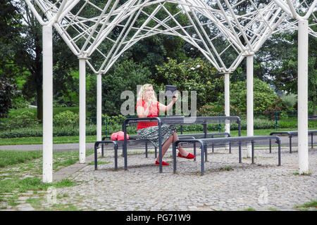 Smiling pregnant woman sitting on a park bench prendre un comprimé avec un selfies Banque D'Images