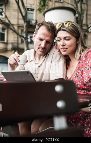 Couple looking at tablet at an outdoor cafe Banque D'Images