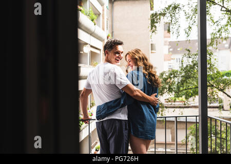 Couple heureux dans des chemises de nuit debout sur balcon hugging Banque D'Images