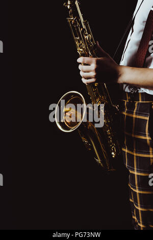 Cropped shot élégant de jeune musicien holding saxophone isolated on black Banque D'Images