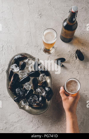 Vue partielle de l'homme avec le verre de bière et les moules avec des cubes de glace dans un bol sur la table d'examen Banque D'Images