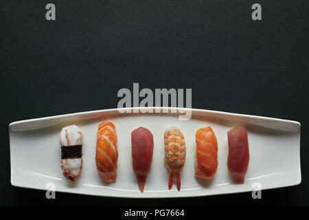 Vue du dessus de l'assortiment de nigiri sushi situé sur la plaque blanche sur la surface sombre Banque D'Images