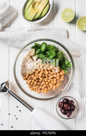 Mise à plat avec des pois chiches et d'autres ingrédients pour l'hoummos dans un bol mélangeur, et d'avocat sur table en bois Banque D'Images