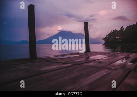 Rose et violet coucher du soleil avec vue sur un volcan d'une jetée en bois sur le lac Atitlan, Guatemala Banque D'Images