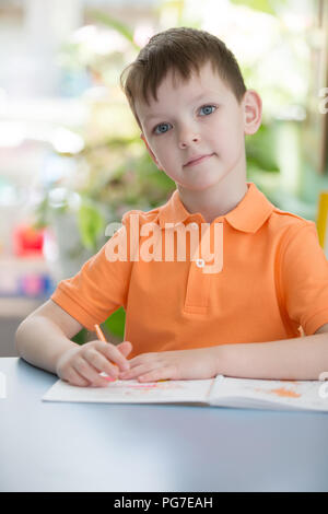 Biélorussie, Minsk, le 29 mai 2018. Le centre de l'école maternelle. Journée portes ouvertes.Un beau garçon de six ans à une table avec un crayon et un bloc-notes Banque D'Images