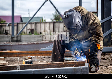 Un jeune homme brun soudeur en uniforme, masque de soudage et des soudeurs, cuir métal soudé avec une machine de soudage à l'arc sur le site de construction, des étincelles bleues Banque D'Images