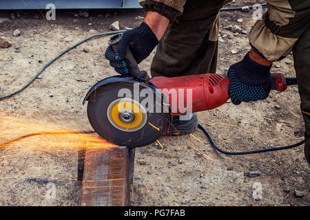 Portrait d'un jeune homme en uniforme brun Soudeur Soudeurs, cuirs, grinder metal une meuleuse d'angle sur le site de construction, orange étincelles voler à th Banque D'Images