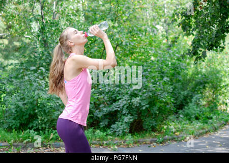 Young sportwoman a terminé son travail et maintenant l'eau potable et souriant dans le parc Banque D'Images