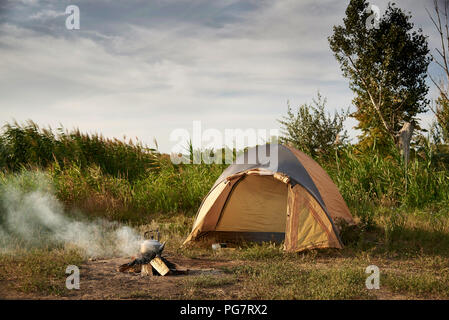 Tente sur la rive du lac près d'un feu brûlant avec une bouilloire. Banque D'Images