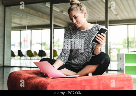 Young businesswoman working in office moderne, assis sur la selle, la lecture de documents Banque D'Images