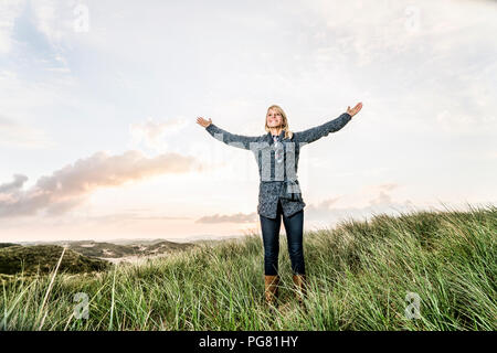 Happy woman standing in dunes avec bras levés Banque D'Images