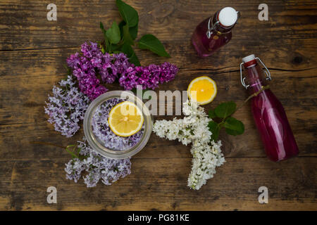 Deux bouteilles en verre de sirop lilas faits maison et les ingrédients sur bois Banque D'Images