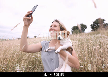 Femme avec chien en tenant avec selfies sur smartphone un champ Banque D'Images