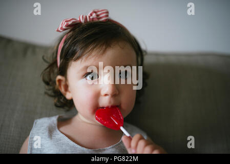 Cute baby girl eating une sucette en forme de coeur à la maison Banque D'Images