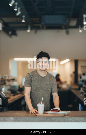 Portrait of smiling man servant des boissons et des gâteaux dans un café-bar Banque D'Images