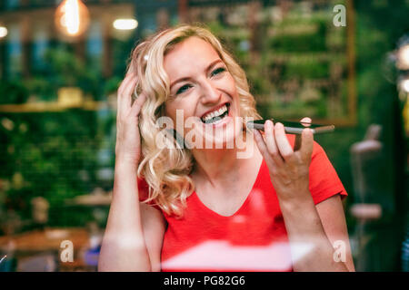 Portrait of laughing woman using smartphone dans un café Banque D'Images