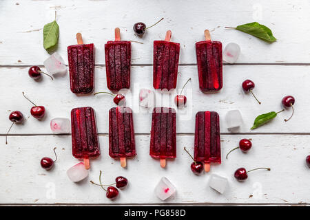 Cerise maison sucettes glacées, des cubes de glace et les cerises sur du bois blanc Banque D'Images