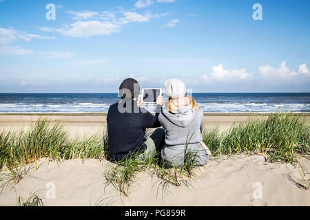 Couple sitting in dunes sur la plage avec tablet Banque D'Images
