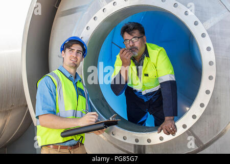Deux travailleurs dans une cuve avec le presse-papiers et talkie walkie Banque D'Images