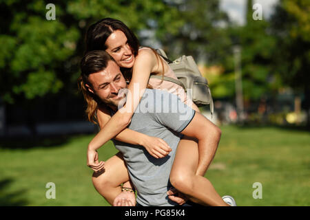Happy man giving girlfriend a piggyback ride in park Banque D'Images