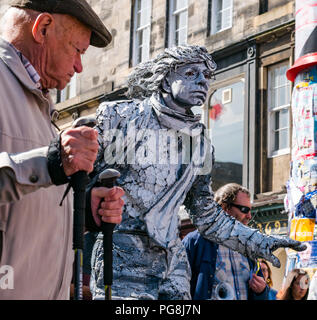 Edinburgh Fringe Festival, Édimbourg, Écosse, Royaume-Uni. 24 août 2018. Le soleil brille sur les festivaliers et un artiste de rue à la Vierge de l'argent liens sponsorisés street sur le Royal Mile. Un vieil homme avec des cannes ressemble à un artiste de rue peint en blanc l'article immobile sur un vélo peint Banque D'Images