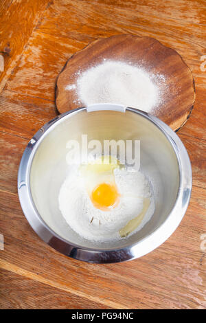 La cuisson de la tarte - tas de farine avec les oeufs cassés dans un bol en acier et la farine sur planche de bois Banque D'Images